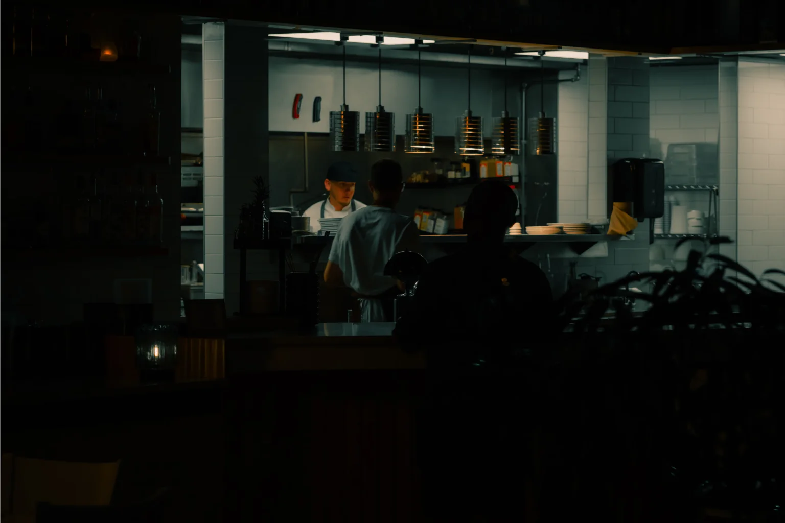 Salón en penumbra con la cocina abierta iluminada al fondo